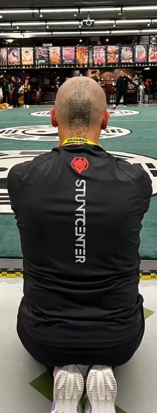 Aang Willians ajoelhado, de costas, na beira do tapete do salão de treino do centro de treinamento de dublês em Pequim, na segunda visita. Ele escreveu que ajoelhar é o maior sinal de respeito a um mestre, a uma linhagem e a um lugar sagrado. 2026, do Instagram dele.