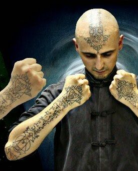 Aang Willians de jaqueta chinesa escura, com os punhos fechados e os antebraços tatuados à frente. Do canal dele no YouTube.