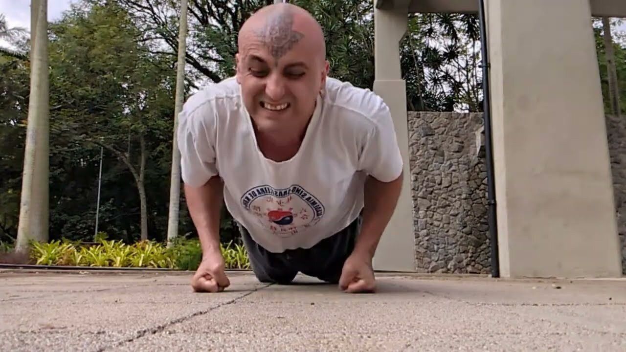 Aang Willians faz flexão sobre os punhos no Parque do Ibirapuera, com a camiseta da Academia Sino-Brasileira de Kung Fu. 9 de maio de 2026, do canal dele no YouTube.