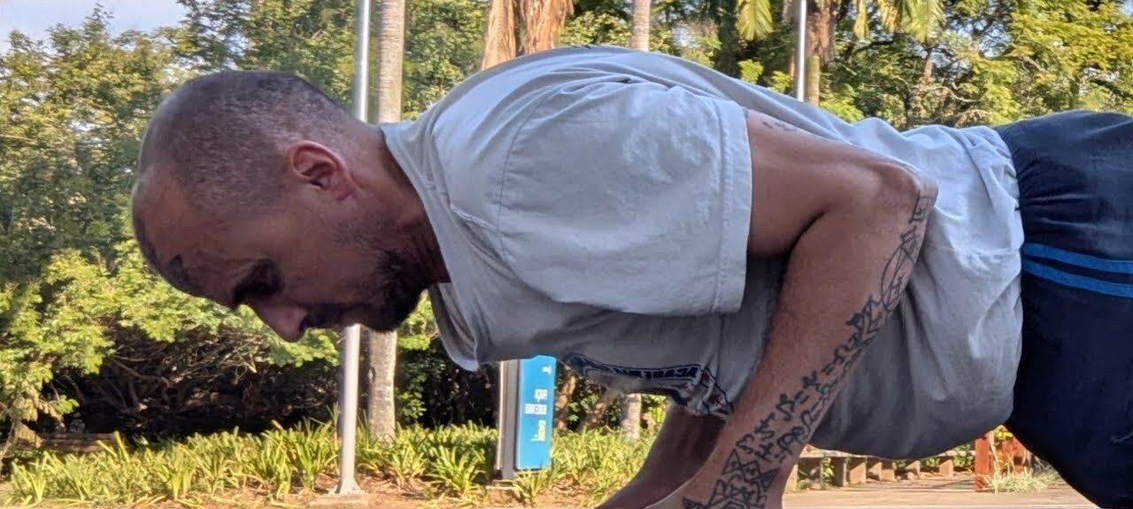Aang Willians faz flexão sobre os punhos no Parque do Ibirapuera, visto de lado. 9 de maio de 2026, do canal dele no YouTube.