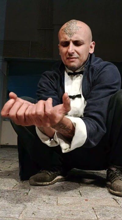 Aang Willians agachado, de jaqueta chinesa escura com punhos brancos, faz um gesto com as mãos. 15 de julho de 2024, do canal dele no YouTube.