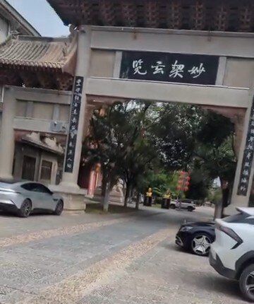 O portão de entrada de Chenjiagou, numa rua de pedra com carros estacionados. 2026, do Instagram dele.