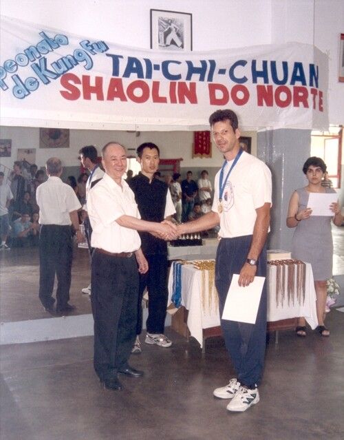 Gilmar Dantas e Chan Kowk Wai se cumprimentam sob uma faixa de tai chi chuan e Shaolin do Norte.